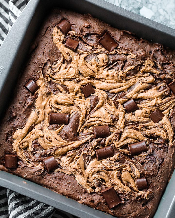 Tray of baked black bean brownies with a swirl of nut butter and chocolate chips.