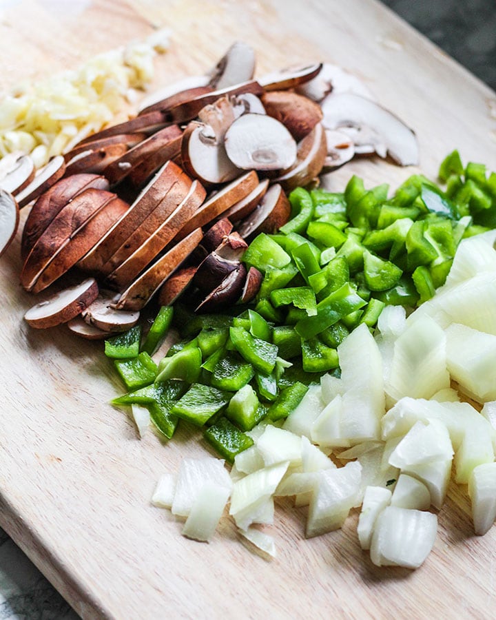 Cutting board with onions, green bell peppers, mushrooms and garlic all sliced up for cooking.