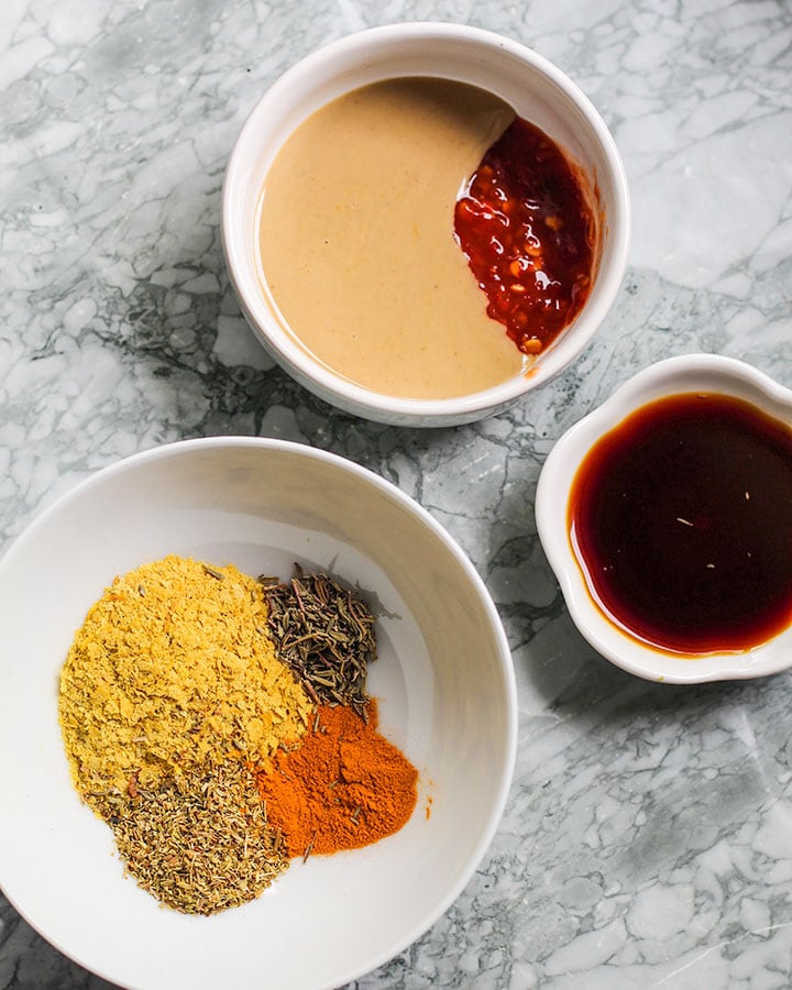 Tahini, garlic chili sauce, soy sauce, nutritional yeast, turmeric, oregano and thyme in cups showing the basic ingredients for this tofu scramble.