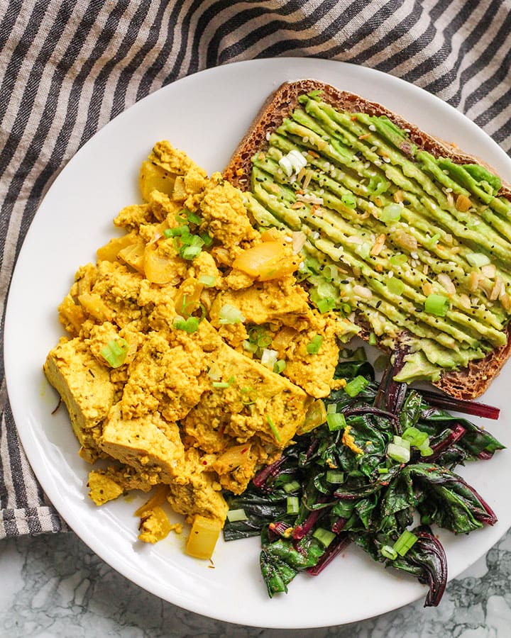 Tofu scramble on a plate with avocado toast, and sauteed beet greens.