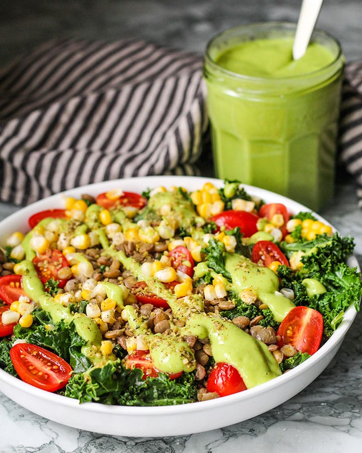 Kale and lentil salad bowl with container of dressing towards the back.