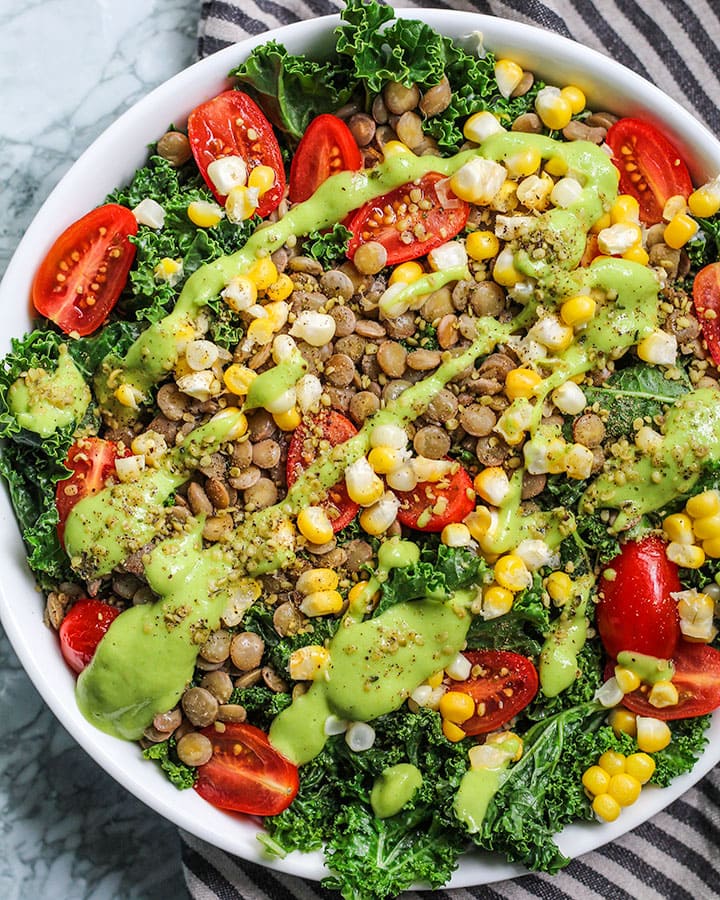 Full lentil, kale salad topped with cherry tomatoes, corn, and green goddess dressing.