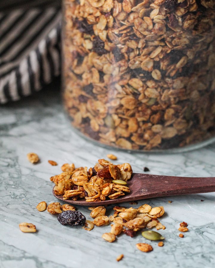 Fresh jar of granola with a spoon of the granola spread out on the surface.