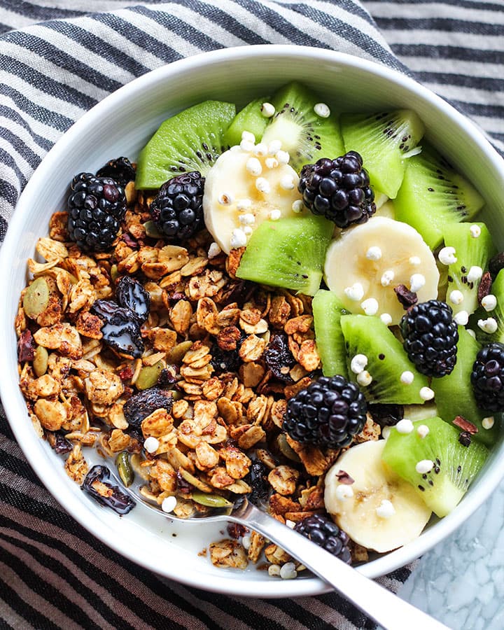 Bowl of granola with milk and topped with kiwi, blackberries and sliced bananas.