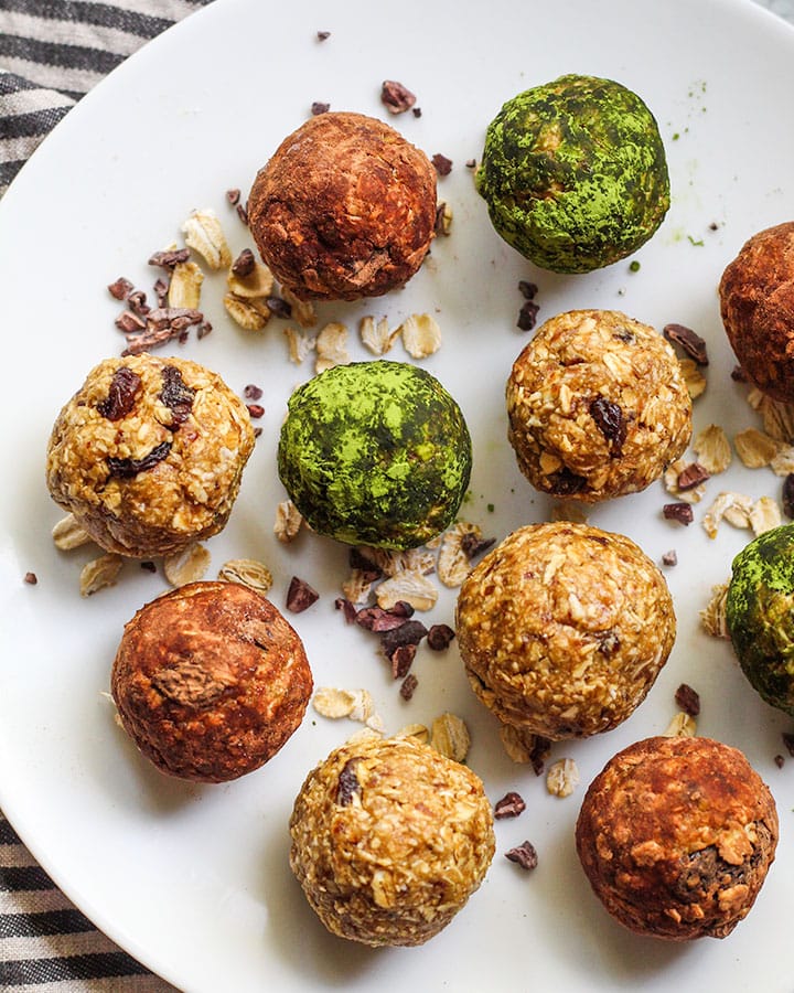 Various energy bites rolled in cocoa powder and matcha powder with a spinkle of rolled oats in the background.