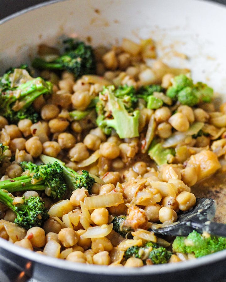 Chickpeas in a pan with peanut miso sauce and broccoli at a side angle.