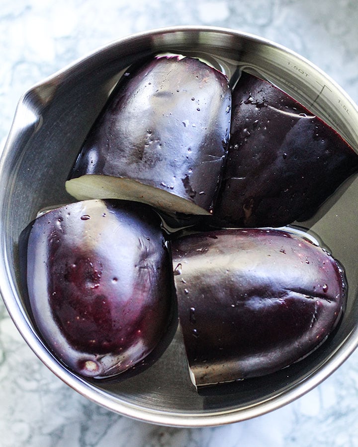 Preparing eggplant by submerging eggplant in salted water bath.