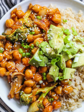 Plate of rice, sweet and sour chickpeas, avocado and topped with diced spring onion and sesame seeds.