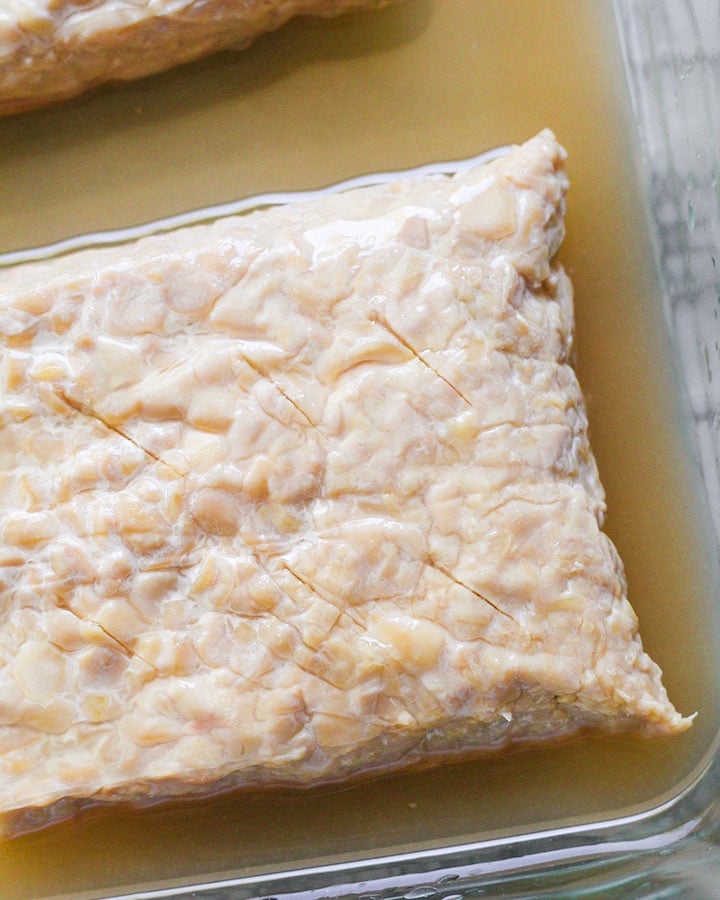 Tempeh block with piercings to allow marinade to penetrate deeper into the tempeh.