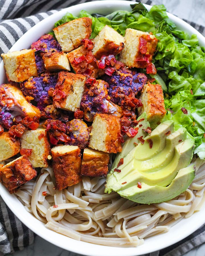 Baked tempeh cut into small pieces and served with noodles, avocado and greens.