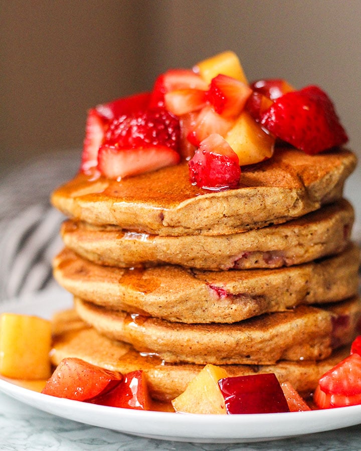 Stack of pancakes topped with strawberries, plums and peaches.