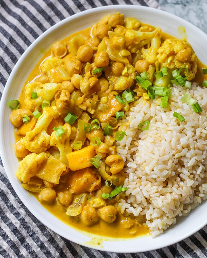 Bowl of coconut mango chickpea curry paired with rice and topped with spring onion.