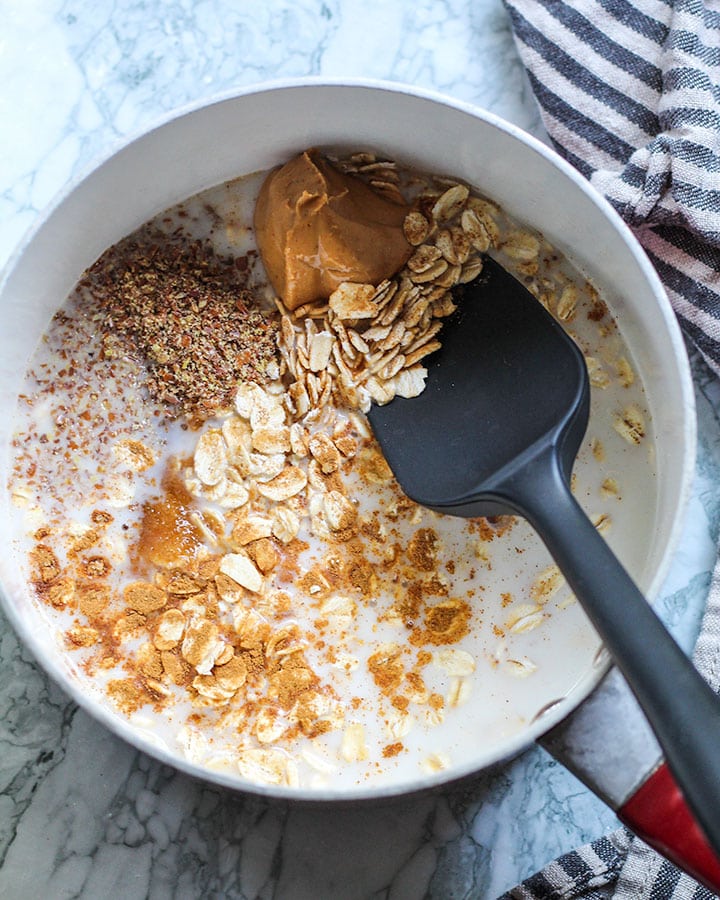 Sauce pan with oatmeal ingredients including rolled oats, cashew butter, ground flaxseed, sugar and cinnamon.