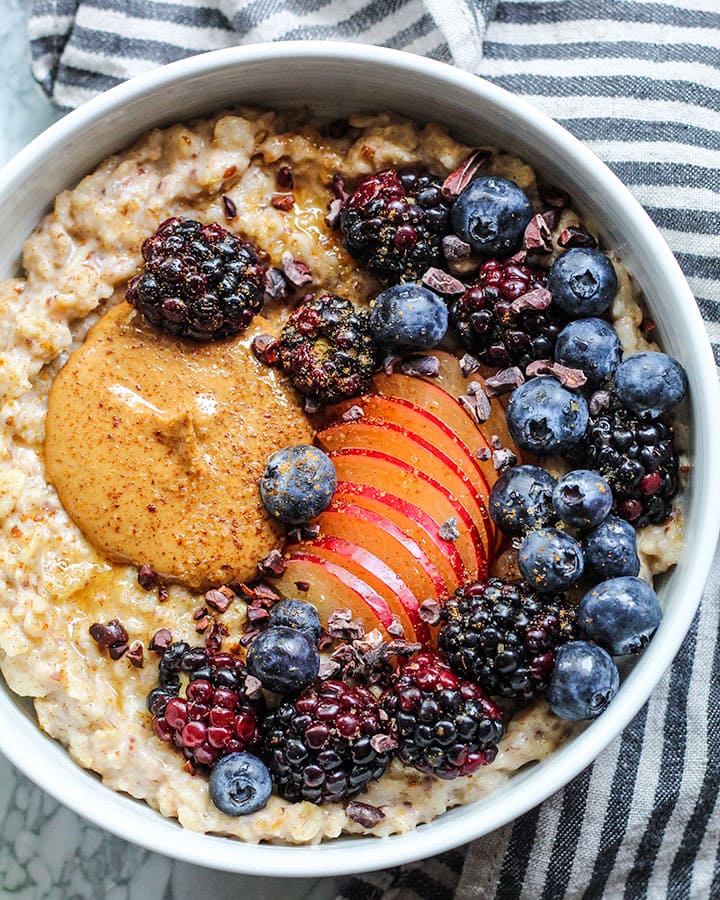 Bowl of snickerdoodle oatmeal topped with berries and plum with a sprinkle of cinnamon and sugar.