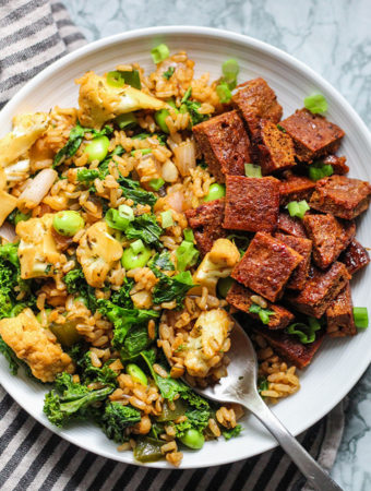 Taking a spoon of fried rice from a plate that is also paired with seitan.