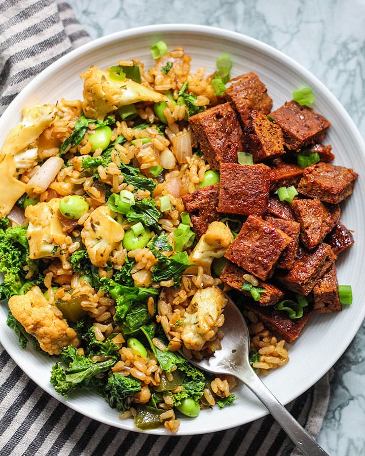 Taking a spoon of fried rice from a plate that is also paired with seitan.