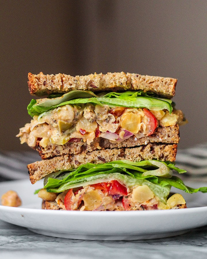 Chickpea salad mixture in between two slices of bread, lettuce and cucumber slices.