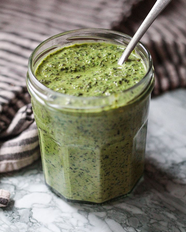 Jar of tahini pesto with spoon ready to serve.