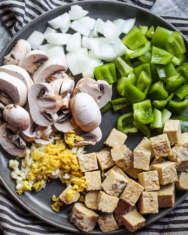 All the ingredients for the black pepper tempeh including diced tempeh, onion, green pepper, sliced mushroom, minced garlic and ginger.