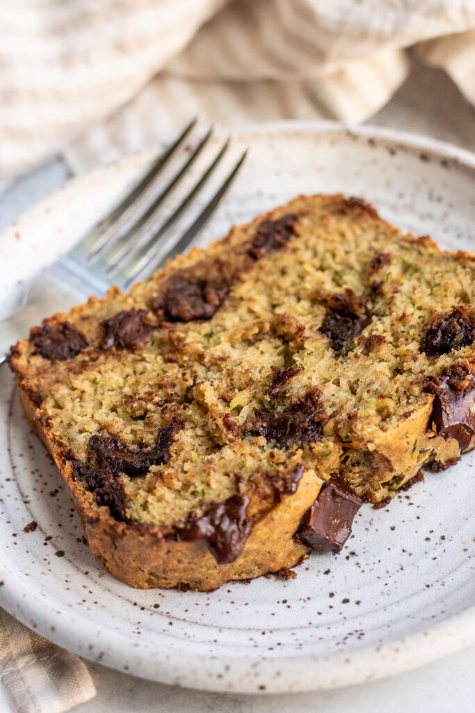 Close up side shot of a slice of zucchini bread with chocolate chips and a fork tucked in the back.