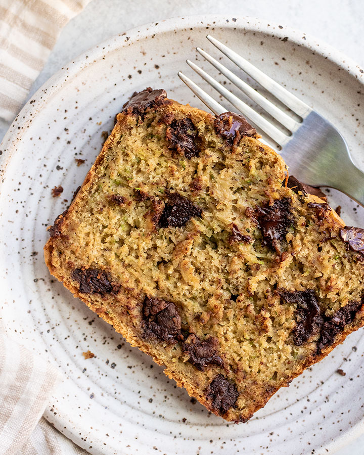 Slice of vegan zucchini bread loaded with melted chocolate chips on a plate with a fork next to it.