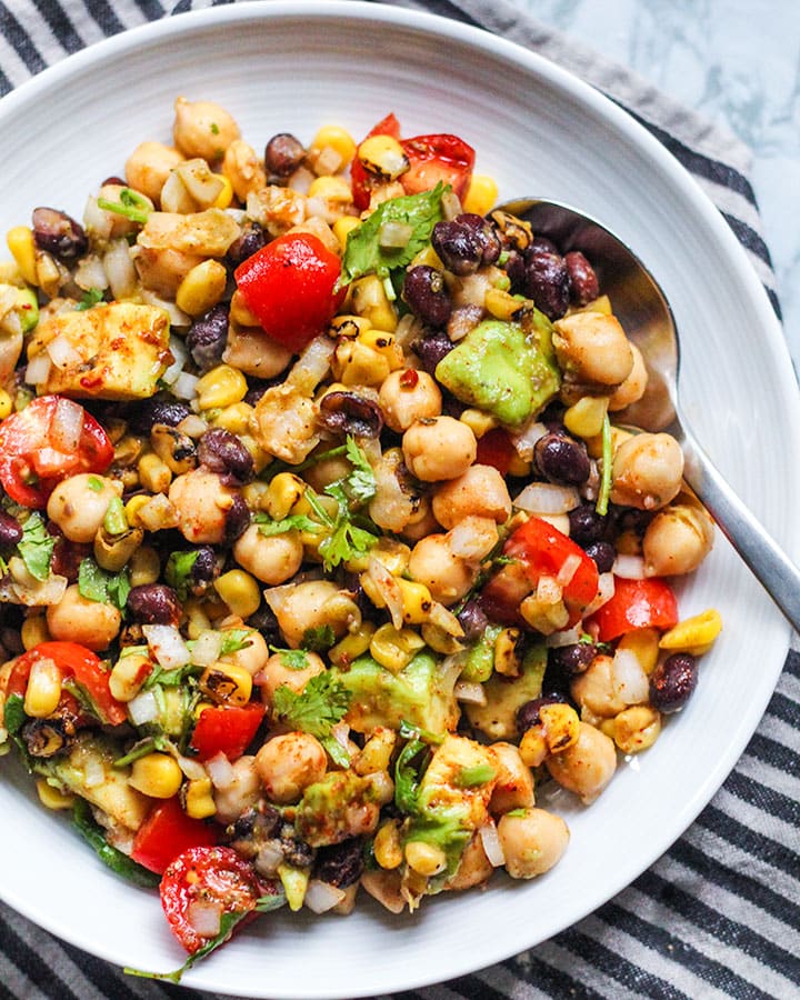 Plate of bean salad with a spoon place into the mixture for eating.