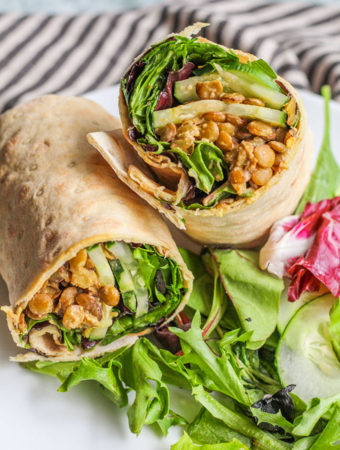 Veggie and lentil stuffed wraps cut in half and placed on a plate with some extra salad and cucumbers.