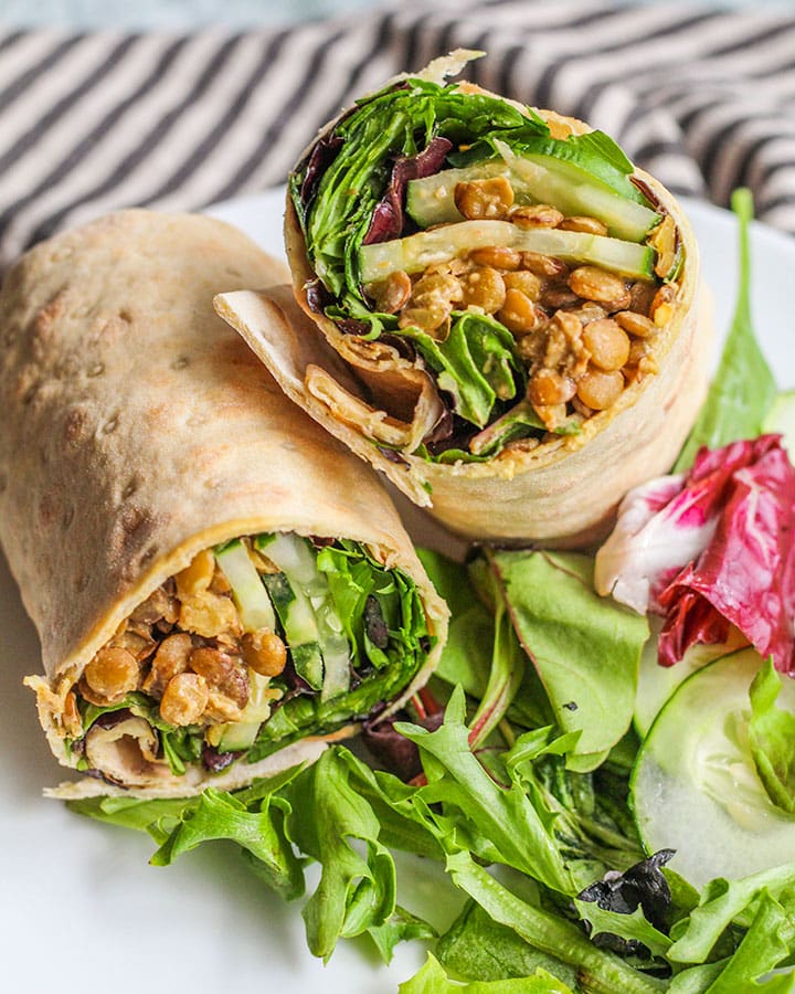 Veggie and lentil stuffed wraps cut in half and placed on a plate with some extra salad and cucumbers.