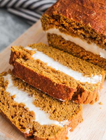 Two slices of pumpkin bread filled with cream cheese sliced away from loaf on a cutting board.