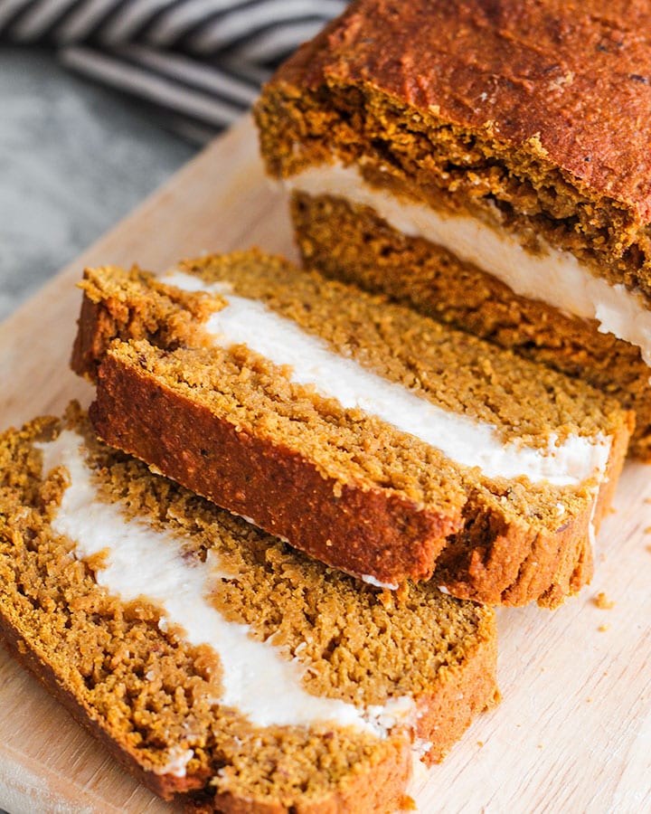 Two slices of pumpkin bread filled with cream cheese sliced away from loaf on a cutting board.