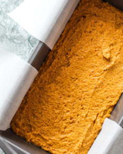 Pumpkin bread batter spread over the bottom of a loaf pan lined with parchment paper.