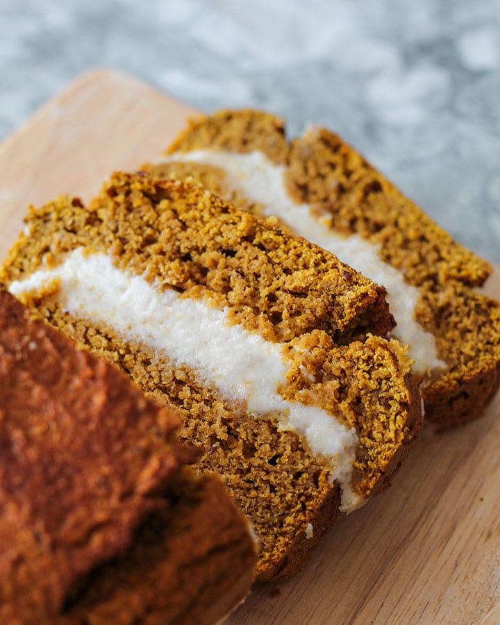 An upward shot of the two slices of pumpkin bread filled with cheese cream cut away from the pumpkin loaf.