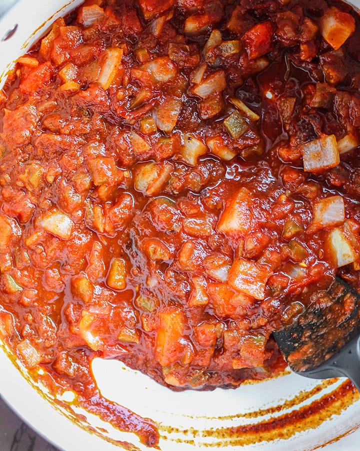 A jar of salsa is added to the large pot with the onions and chipotle peppers.