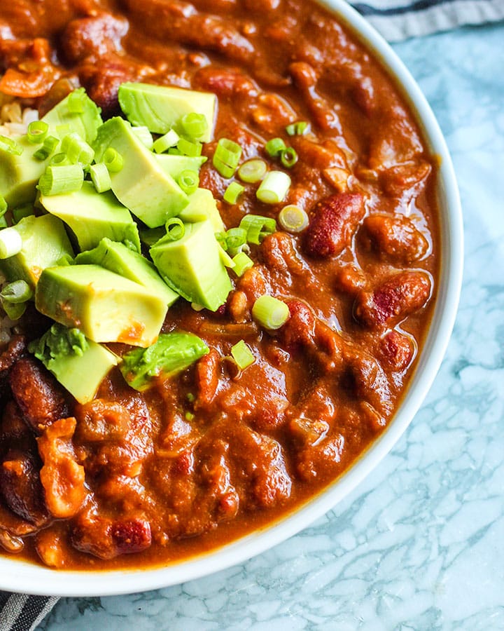 Plate of pumpkin chili topped with avocado and spring onion.