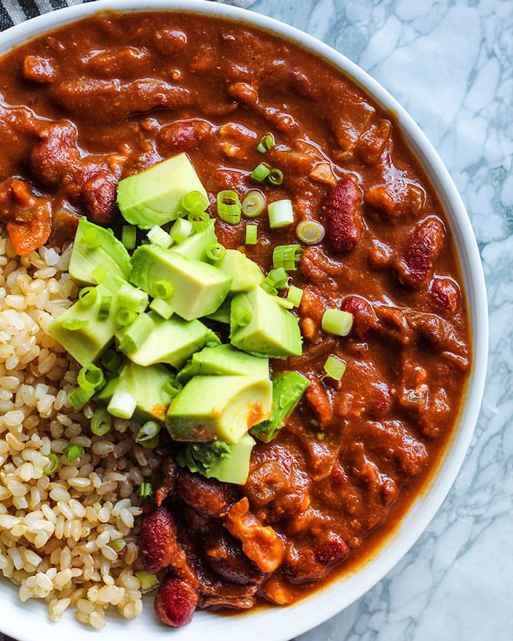 Pumpkin chili served in a bowl with brown rice, avocado and spring onion.