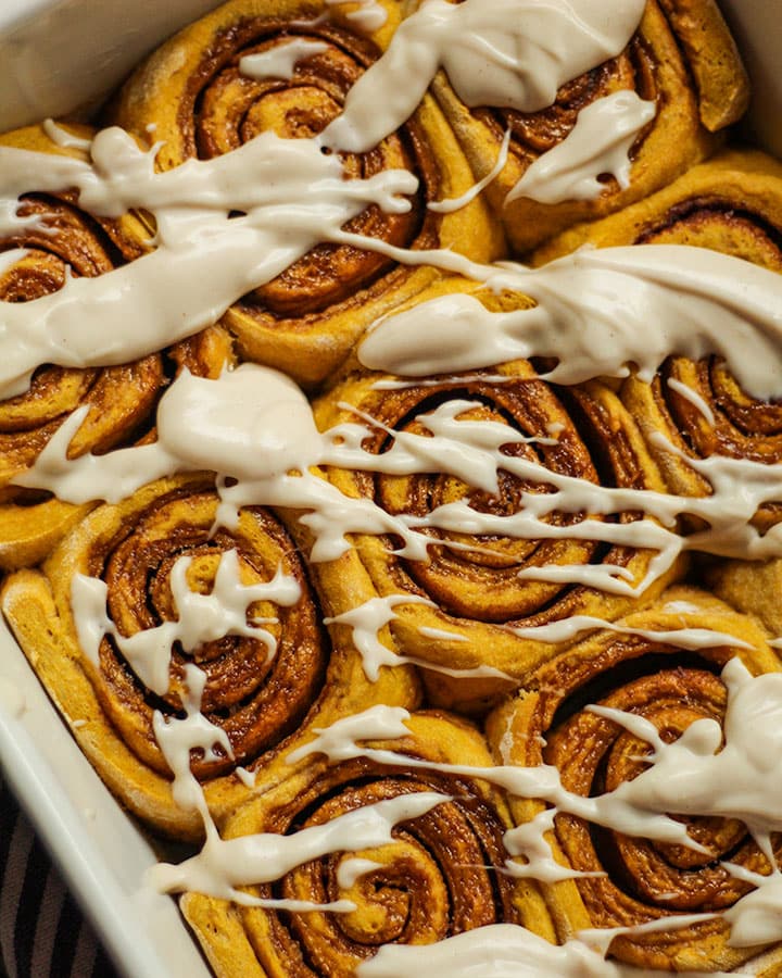 Freshly baked baking pan of cinnamon rolls with cream cheese frosting drizzled over top.