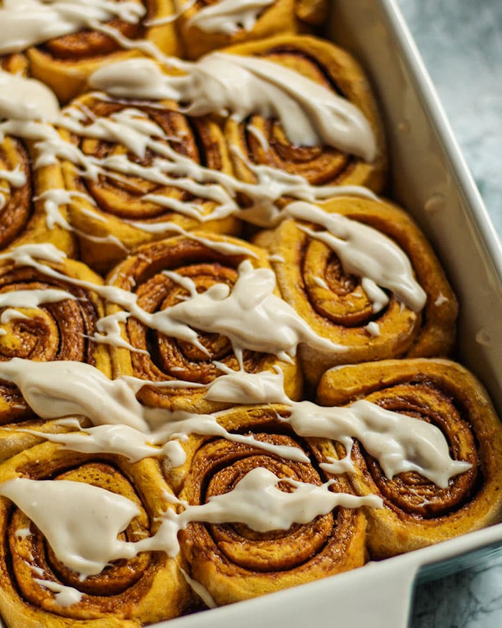 An angled shot looking down at a tray of cinnamon rolls drizzled with cream cheese frosting.