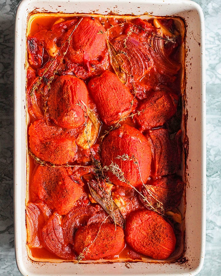 Baking dish of roasted tomatoes, garlic, red onion, thyme and sazon.