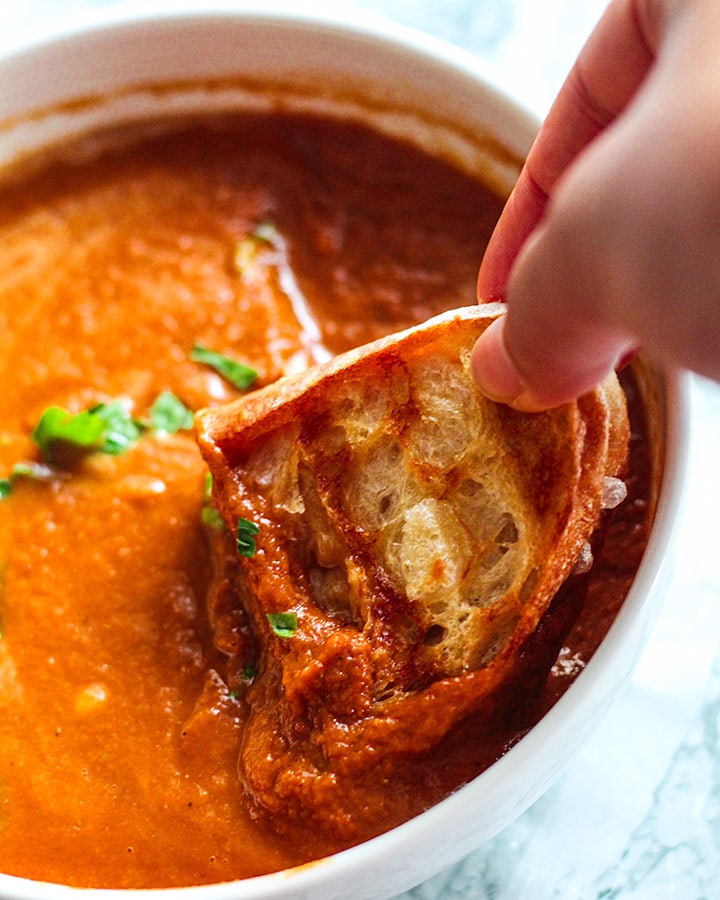 Dipping some vegan grilled cheese bites into some creamy roasted tomato soup.