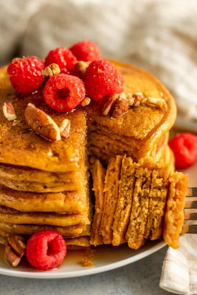 Freshly cut stack of pancakes with a forkful of pancakes laid next to the plate.