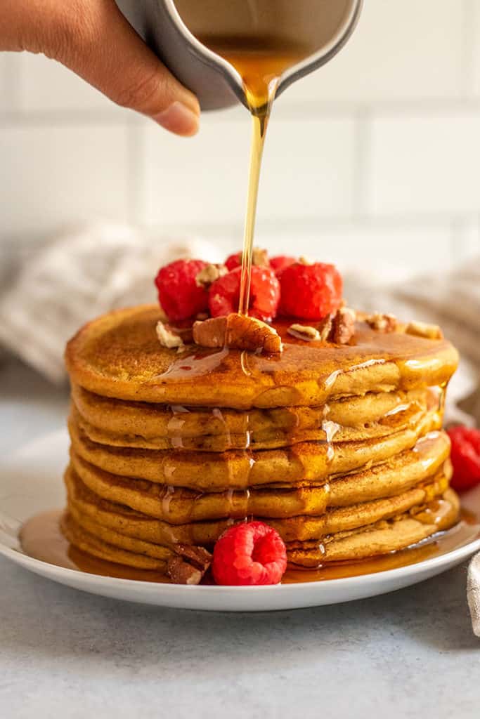 Pancakes getting a fresh pour of maple syrup on top.