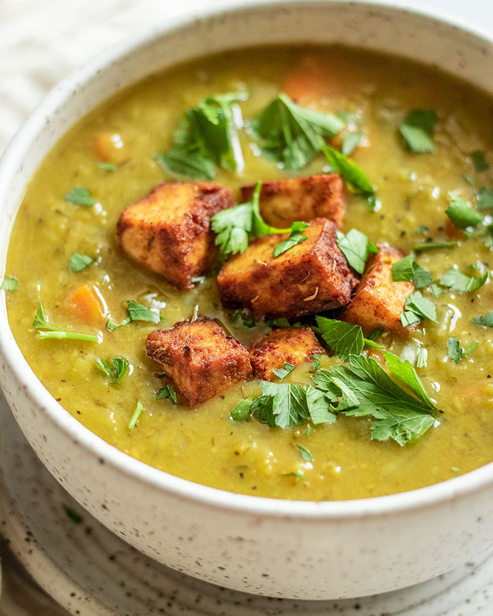 Side view of bowl of soup topped with baked tofu and parsley.