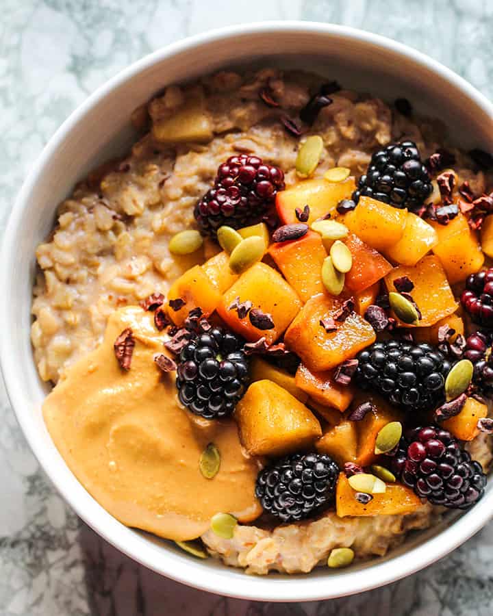 A bowl of apple oats topped with extra sauteed apples, blackberries and peanut butter.