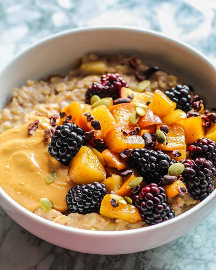 Side view of a bowl of apple oats topped with blackberries, apples and peanut butter.