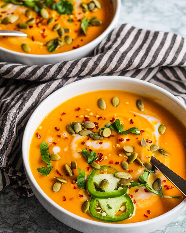 Side view of butternut squash soup bowls topped with spicy toppings like pepper flakes and jalapeno