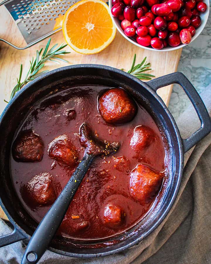 Close up of pot of cranberry chili meatballs with cranberry garnishes and orange slices next to the pot.