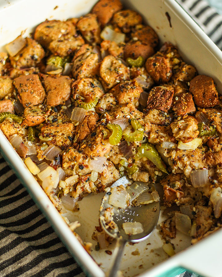 A scoop of bagel stuffing removed with a spoon resting in the empty spot of the baking dish.