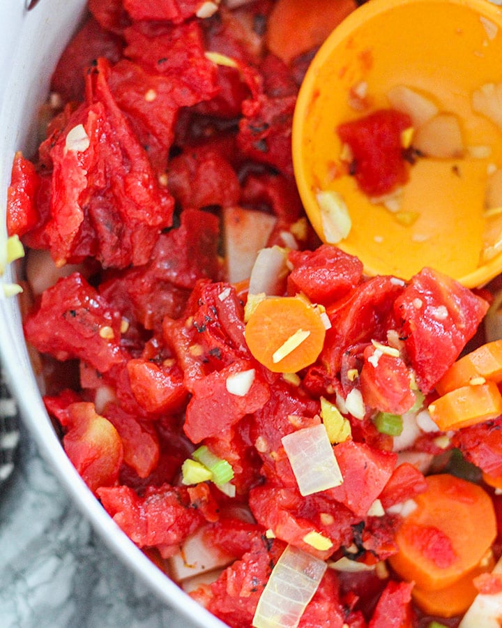 Fire roasted tomatoes added to a pot with sautéed carrots, onions, celery, garlic and ginger.