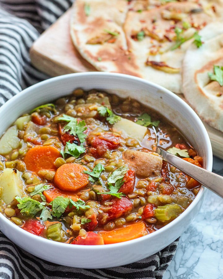 Vegetable loaded lentil soup in the front with pita on a cutting board in the back.