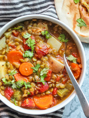 Bowl of lentil soup with a spoon pointing towards the viewer and pita in the backgroun.